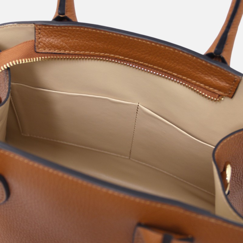 Interior view of a tan leather handbag with beige lining, showing a zippered top edge and a large main compartment