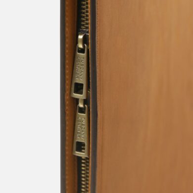 Close-up of two brass zipper pulls on a brown leather bag, partially open, showing the zippers side by side.