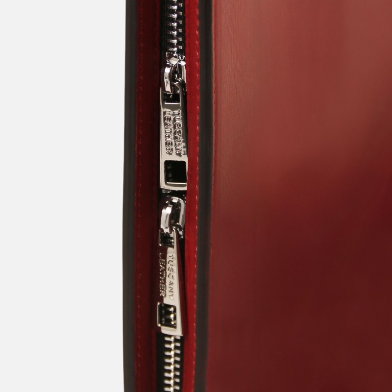 Close-up of a silver metal zipper running along a red leather surface on a bag or case.