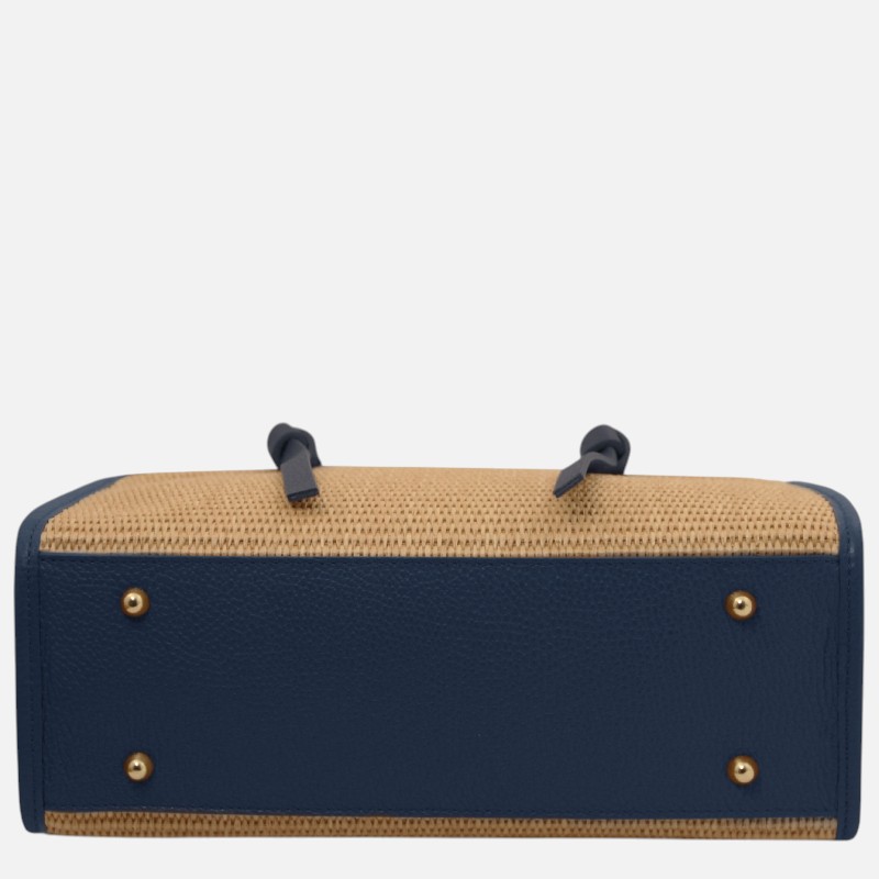 Bottom view of a navy blue leather bag with tan woven straw sides, gold studs, and two dark strap handles.