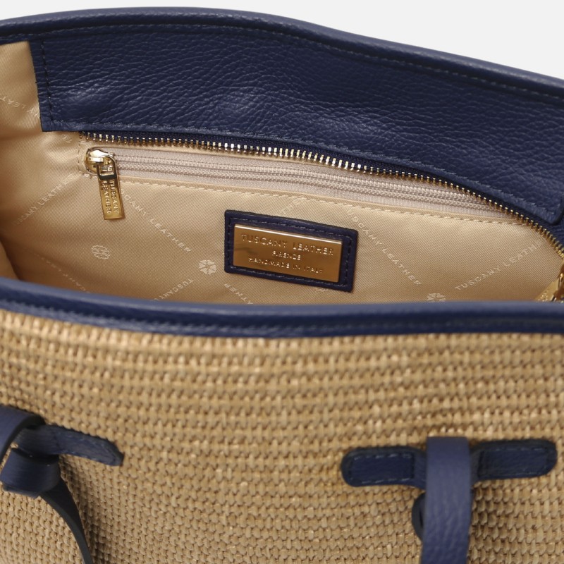 Interior of a navy leather-trimmed straw tote with a gold zipper and tan lining; brand plaque visible inside.