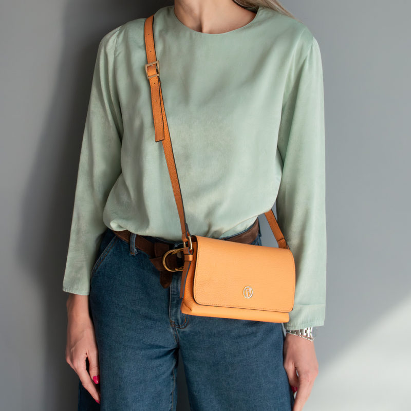 Woman wearing a mint green blouse and blue jeans with a tan crossbody bag worn across the chest area.