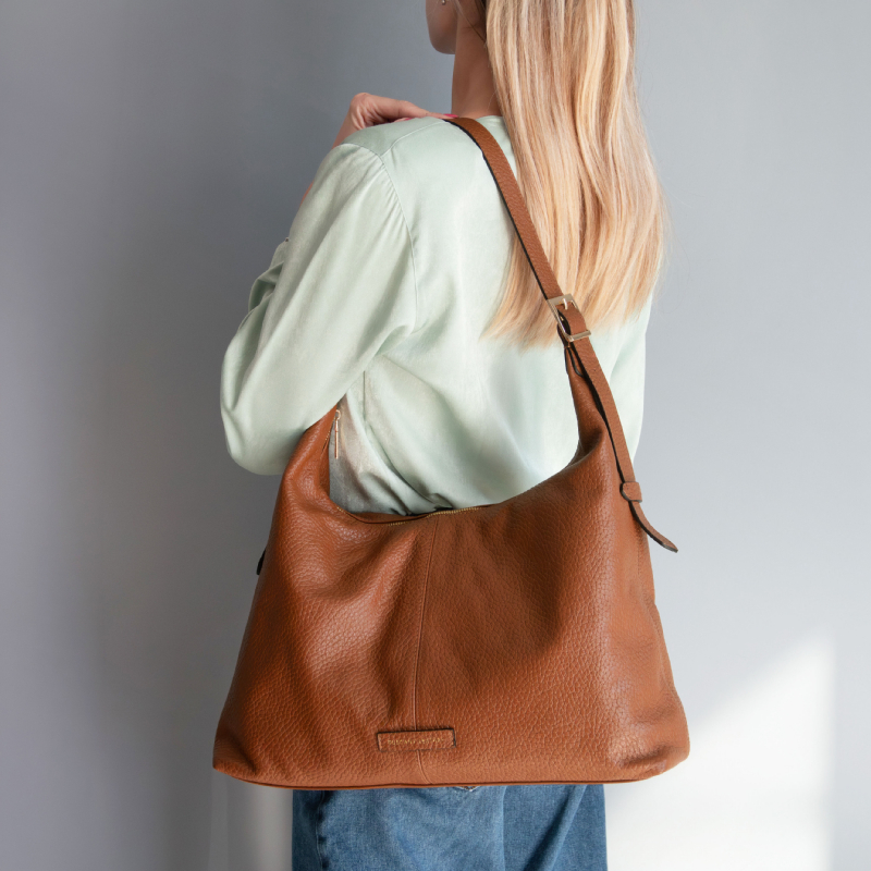 Brown pebbled leather shoulder bag worn crossbody on a person in a light green top, back view.