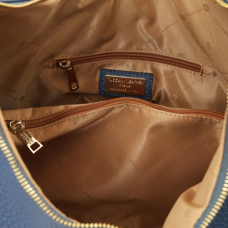 Interior of a blue handbag showing brown lining, two zipper pockets, and a small blue brand tag inside.