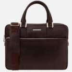 Dark brown leather briefcase with two top handles and a detachable shoulder strap, front zip pocket visible.