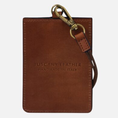 Brown leather card holder with a small attached strap and brass hardware, stamped 'TUSCANY LEATHER HANDMADE IN ITALY'.