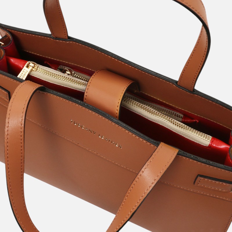 Brown leather handbag with gold zipper interior and red lining, showing brand Tuscany Leather.