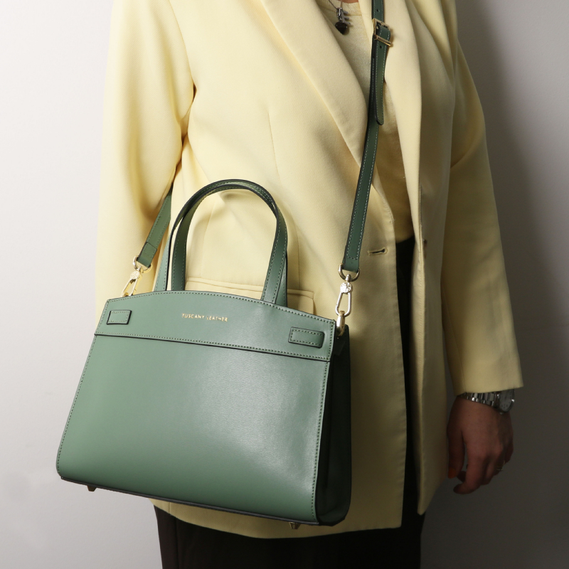Mint green handbag with top handles and a detachable strap carried by a person in a pale yellow blazer/coat.