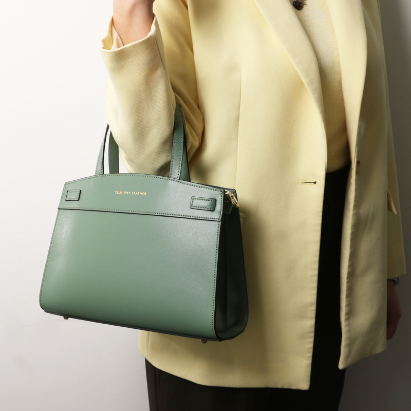 Pastel green structured handbag with two top handles carried by a person in a pale yellow blazer/coat.