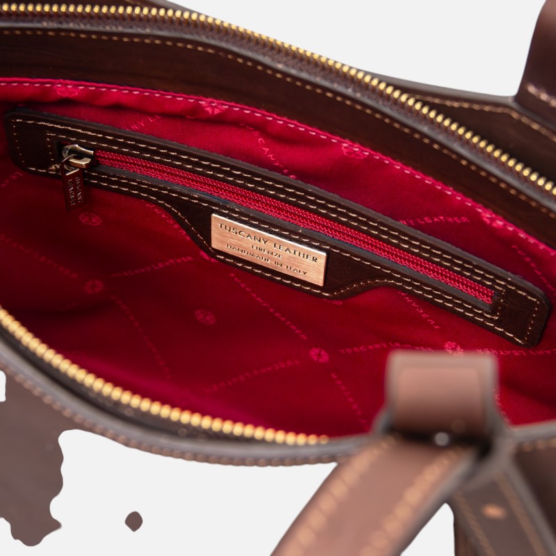 Inside view of a brown leather bag with red lining and a zippered pocket featuring a Tuscany Leather label.