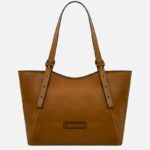 Tan leather tote bag with two long straps and a small front label, empty and standing upright against a light background.