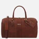Brown leather travel duffel bag with two top handles, metal hardware, and a branded luggage tag.