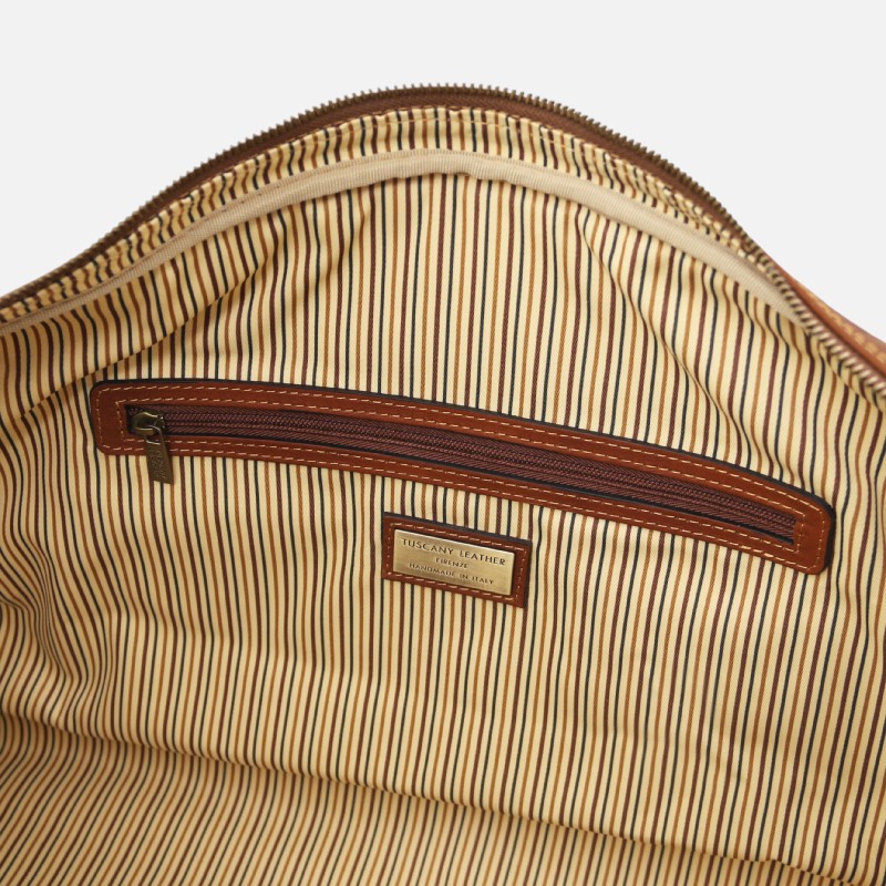 Interior of a striped fabric bag with a brown leather zipper pocket and a Tuscany Leather brand label inside.