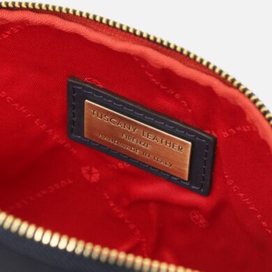 Inside a red-lined zippered bag showing a navy leather tag with a copper plate reading 'Tuscany Leather' and 'Handmade in Italy'